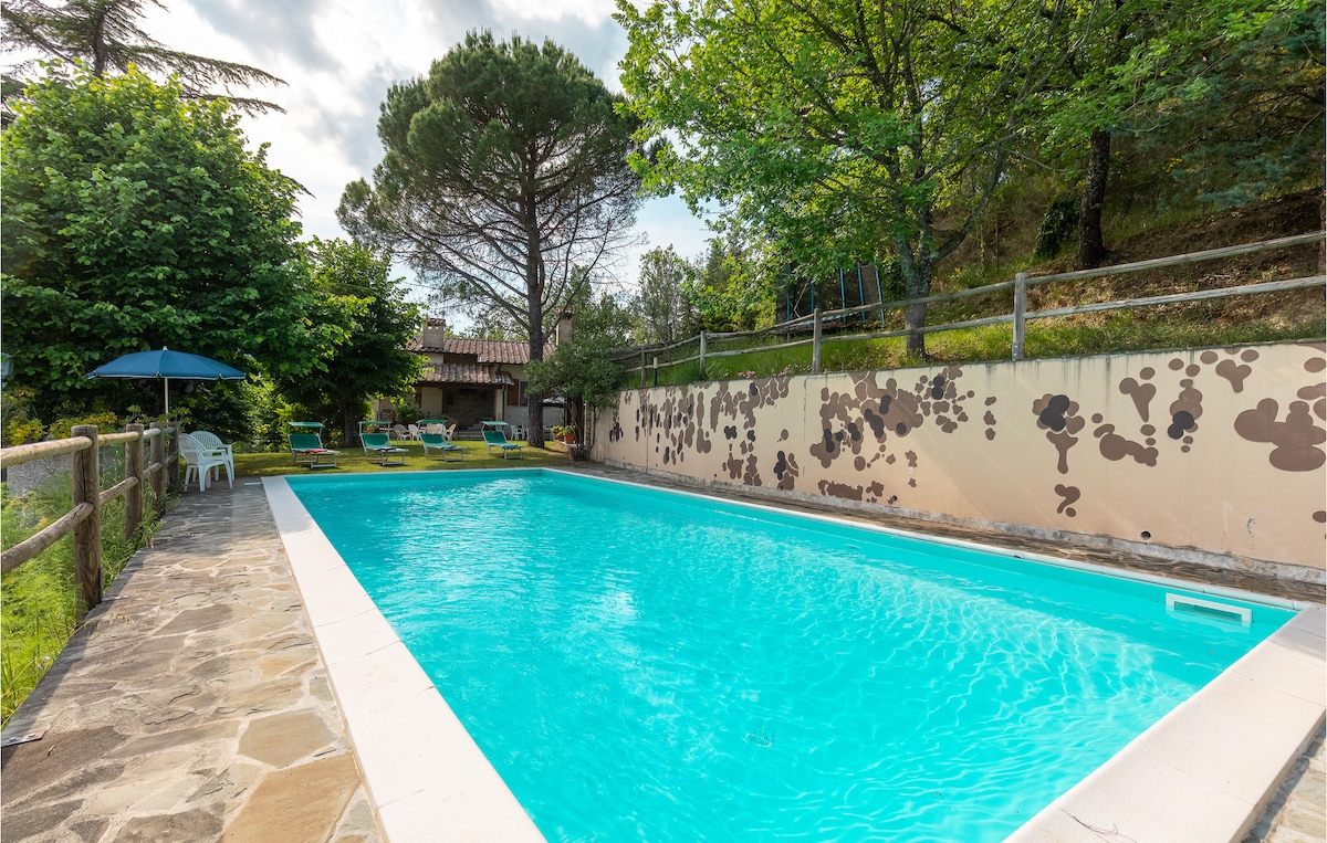 A private outdoor pool is surrounded by lush greenery and trees, creating a serene environment. Sun loungers and an umbrella are visible nearby, while a stone pathway leads around the pool area, providing easy access to the surrounding garden.