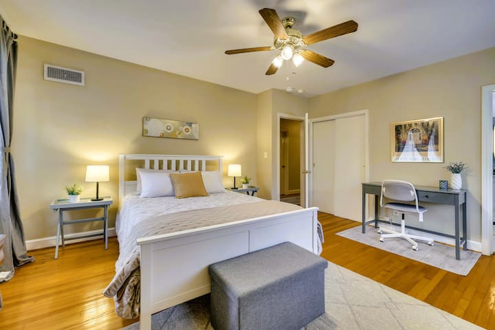 Dormitorio soleado con cama tamaño queen, espacio de trabajo y ventilador de techo.