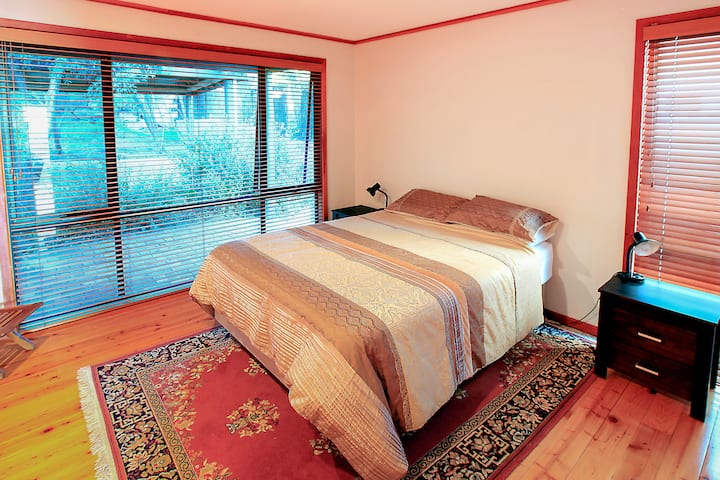 Un primer dormitorio sereno y espacioso con una cómoda cama tamaño king y grandes ventanales con vistas al exuberante entorno.