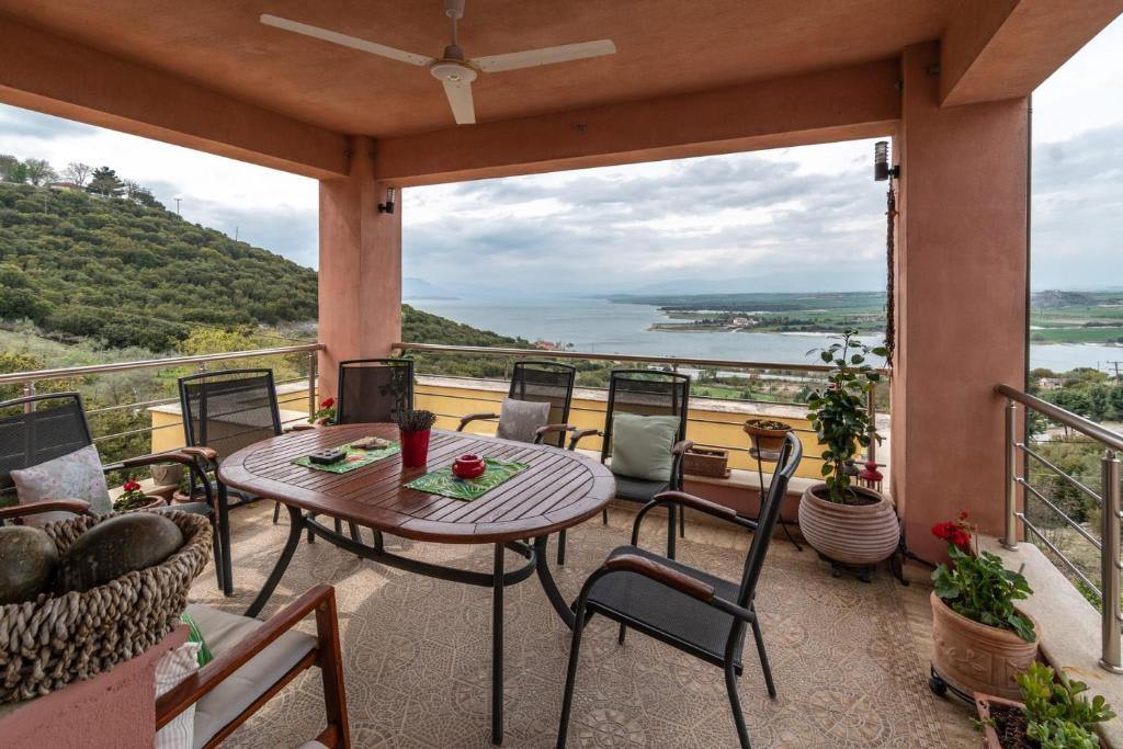 An outdoor terrace showcases a round wooden table surrounded by six chairs, overlooking a scenic view of water and greenery. Potted plants add a touch of color to the space, while a ceiling fan is situated above for comfort.