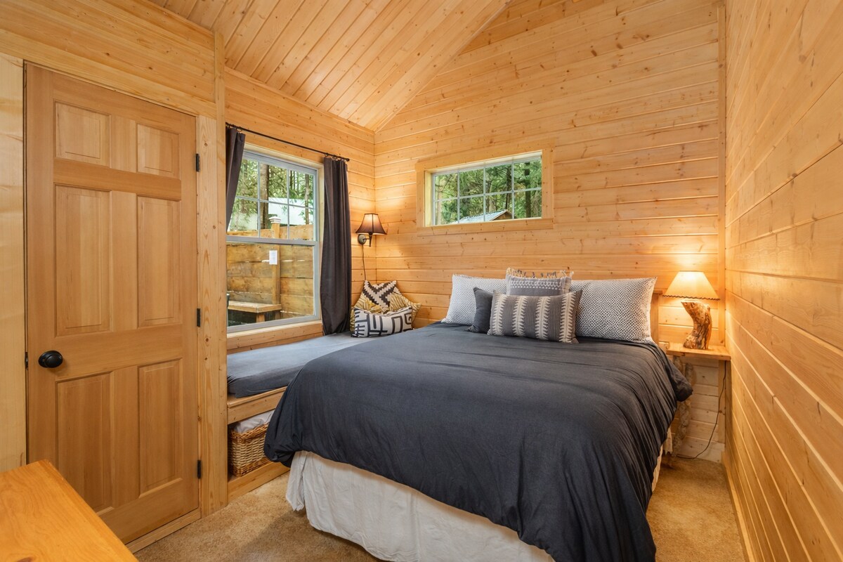 Your cozy wooden retreat awaits with warm pine walls and forest views through charming windows, perfect for peaceful nights.