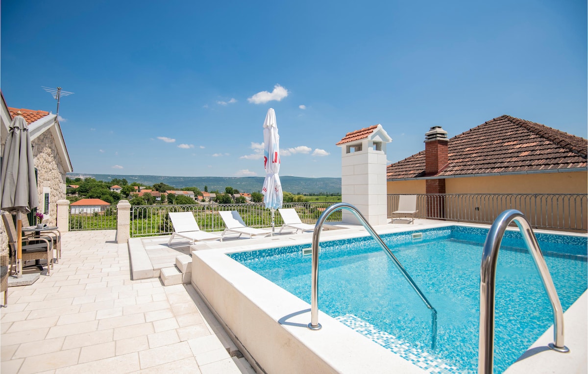 A private outdoor pool is surrounded by a spacious terrace, featuring several lounge chairs for relaxation. A large umbrella provides shade, while scenic views of the countryside and vineyards are visible in the background. The area is sunlit, enhancing the tranquil setting.