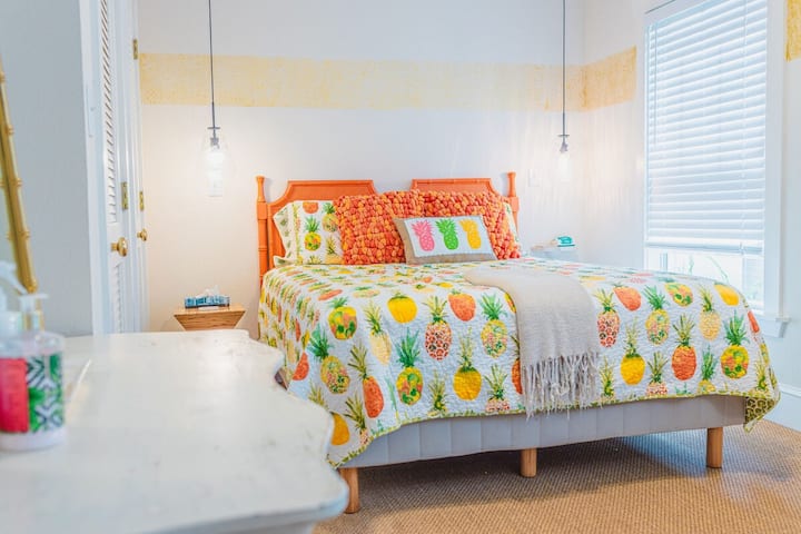 This lively bedroom boasts a tropical pineapple theme with vibrant bedding and orange accents. The playful décor and bright colors create an inviting, sunny space perfect for relaxing and enjoying a cozy stay.