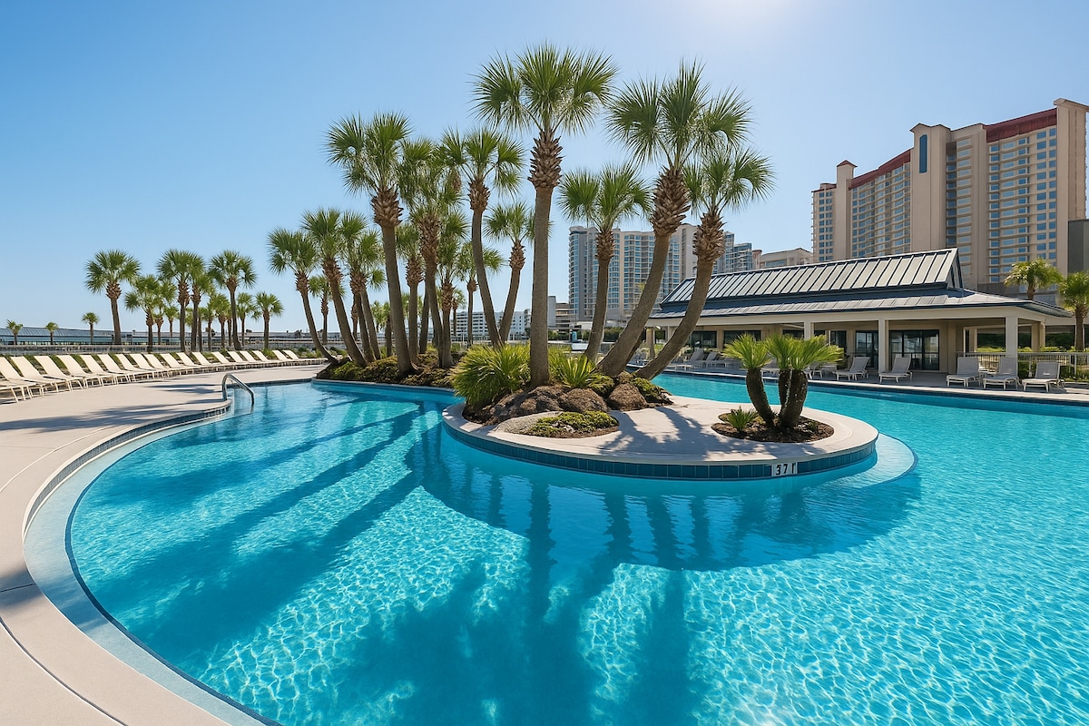 A lagoon-style pool is surrounded by lush palm trees and tropical landscaping. The clear blue water reflects the sky, inviting relaxation. Sun loungers are arranged on the pool deck, with a nearby shaded area featuring a building that offers amenities for guests.