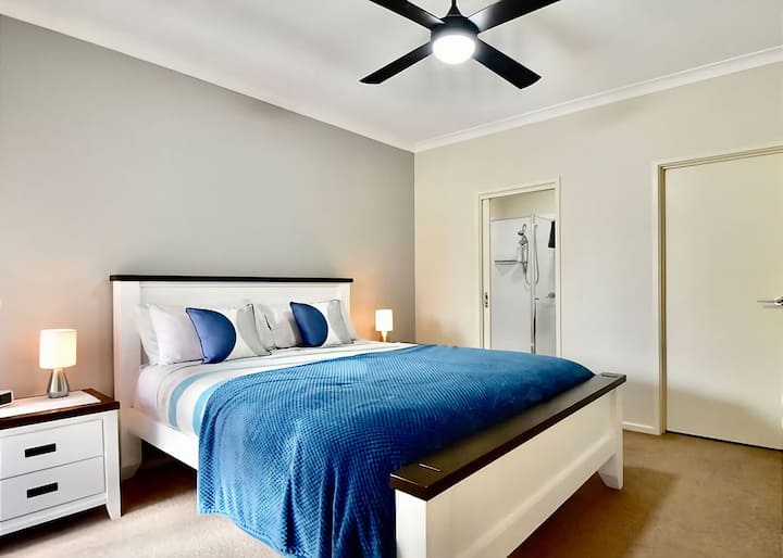 ห้องนอนใหญ่พร้อมเตียงควีนไซส์และห้องน้ำในตัวพร้อมฝักบัวโต๊ะเครื่องแป้งและโถสุขภัณฑ์