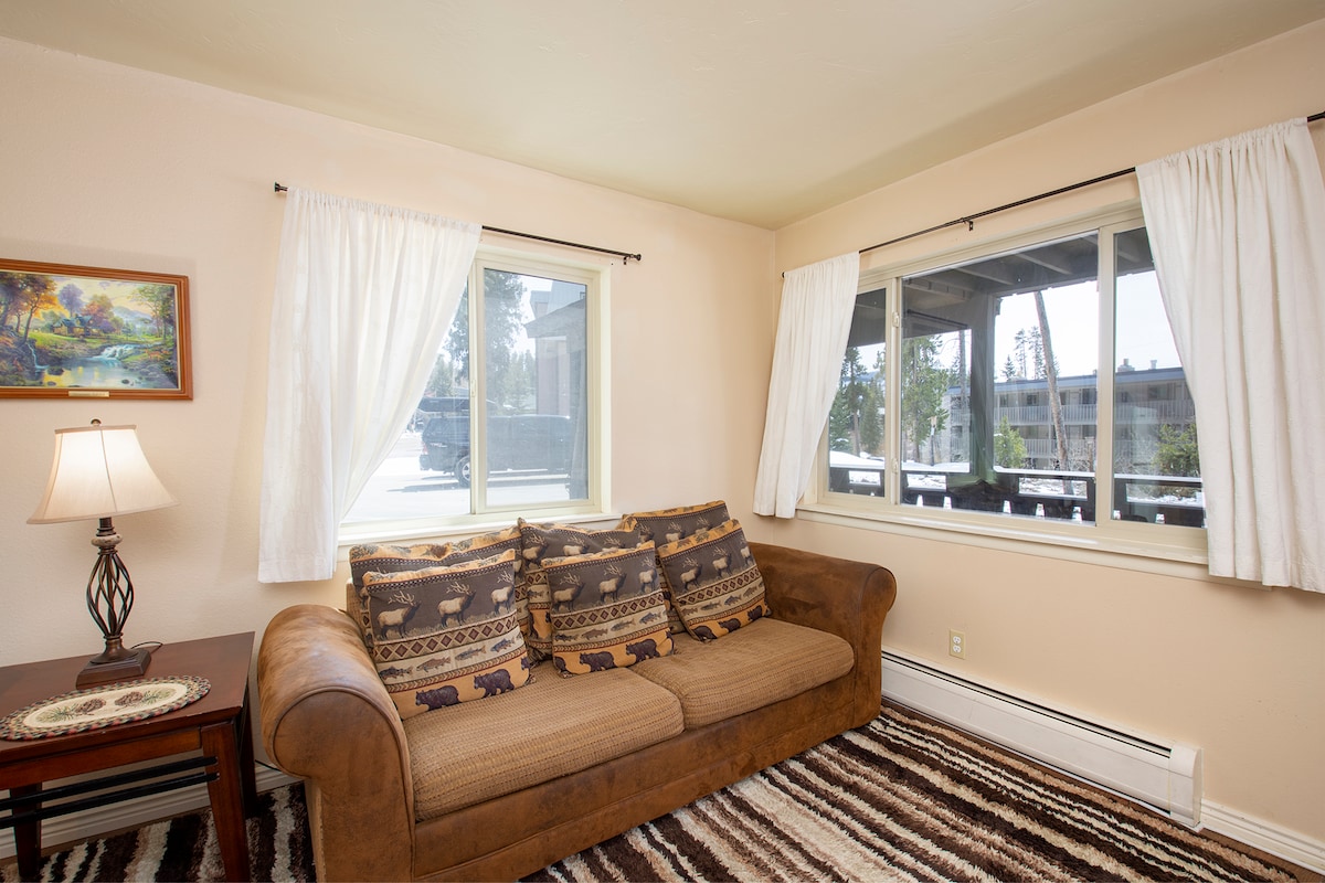 Settle into your cozy corner living room, where soft natural light filters through white curtains and rustic charm meets modern comfort.