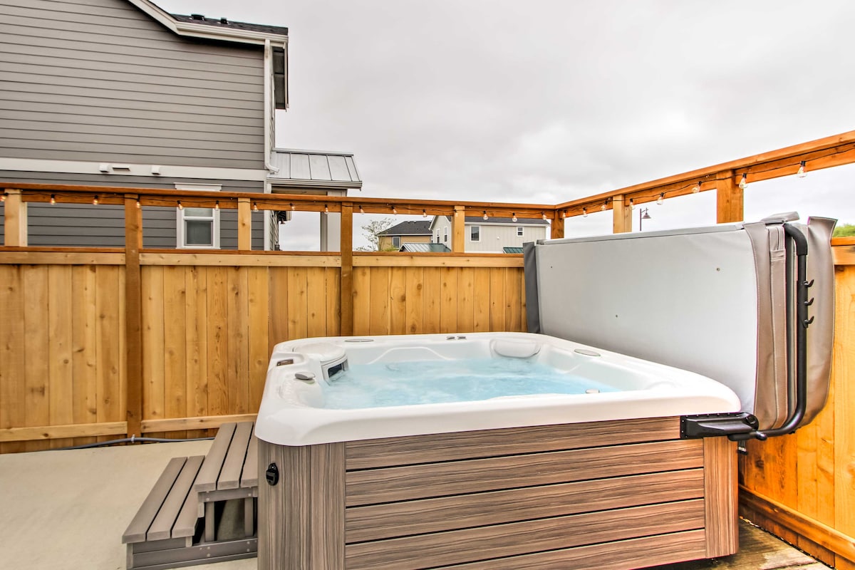 The private hot tub is situated on a patio, surrounded by a wooden fence for privacy. The tub features a white surface with a light blue water interior, and steps lead up to it. An overcast sky is visible above.