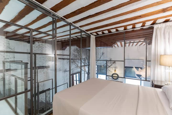 Chambre au deuxième étage, avec un lit double, dans un compartiment avec un mur de verre de style industriel.