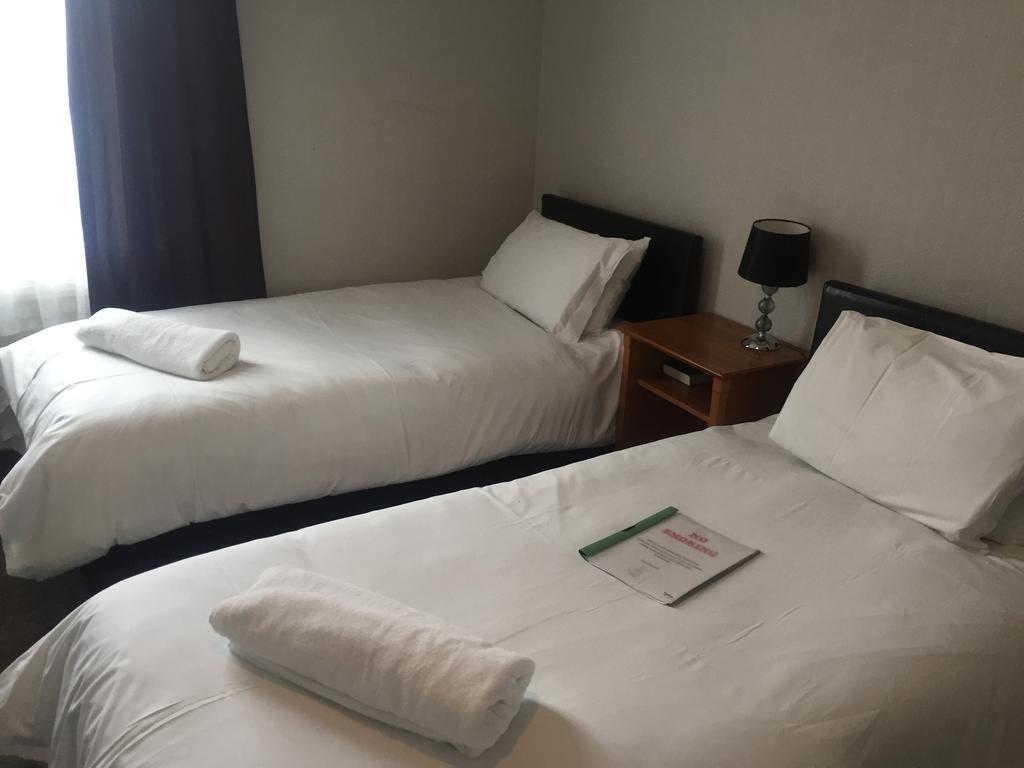 A sleeping area is presented with a double bed and a single bed, each featuring crisp white linens and neatly arranged towels. A small bedside table holds a lamp, and natural light enters through a window, enhancing the serene ambiance.