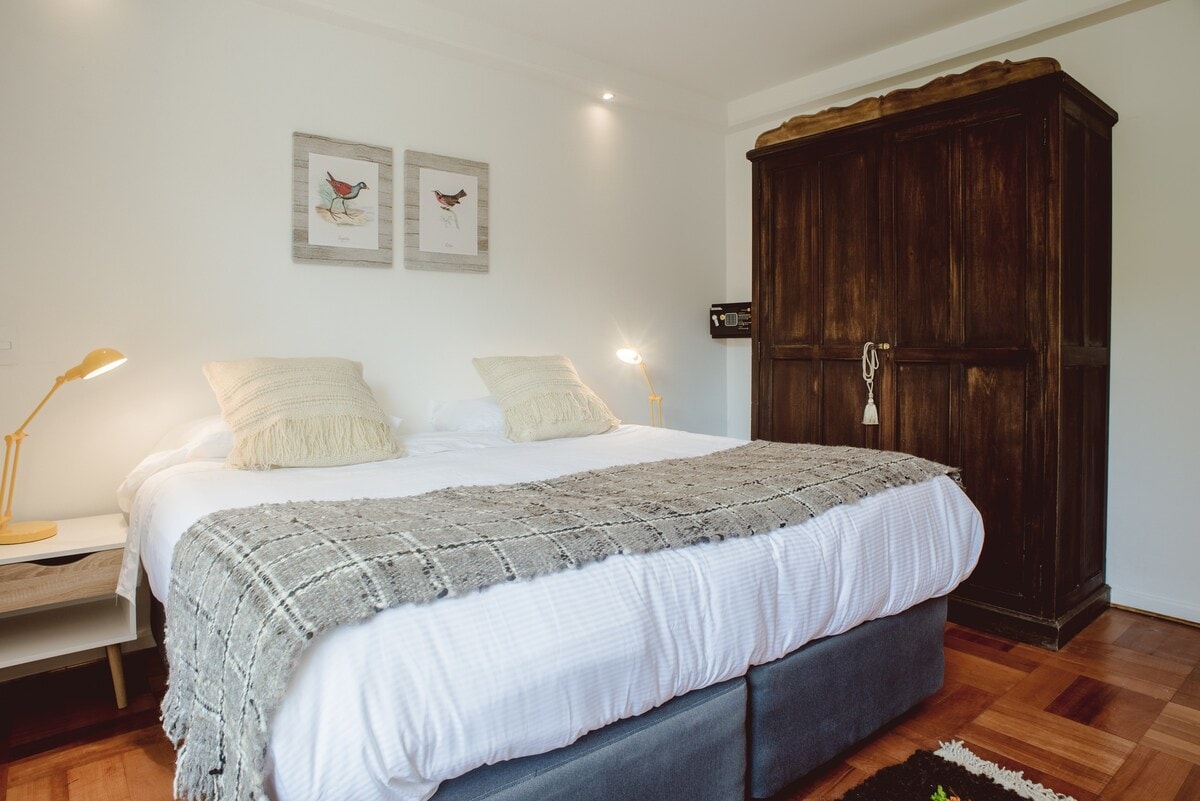 Მყუდრო საძინებელი პლუშის საწოლით, ჩიტების მომხიბლავი ხელოვნებითა და სოფლის ხის აქცენტებით მშვიდი დასვენებისთვის.