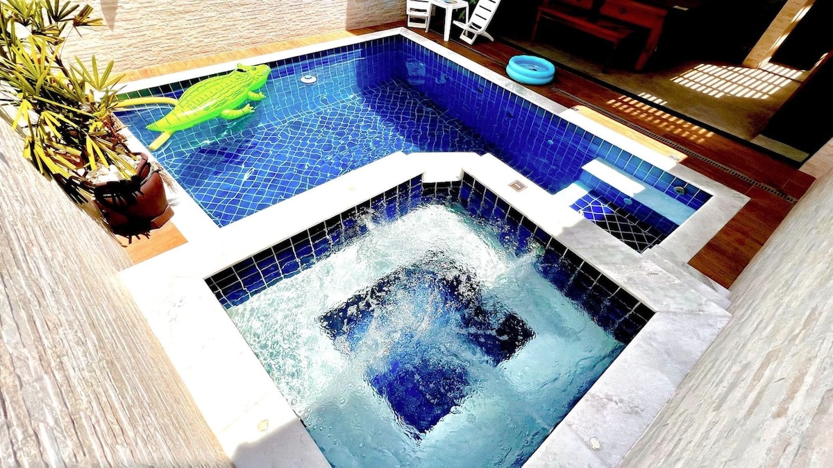 A private pool area is highlighted, featuring a large swimming pool with a vibrant blue tile design. Adjacent, a hot tub is visible, creating a soothing atmosphere. Surrounding greenery and outdoor seating complement the relaxing space.