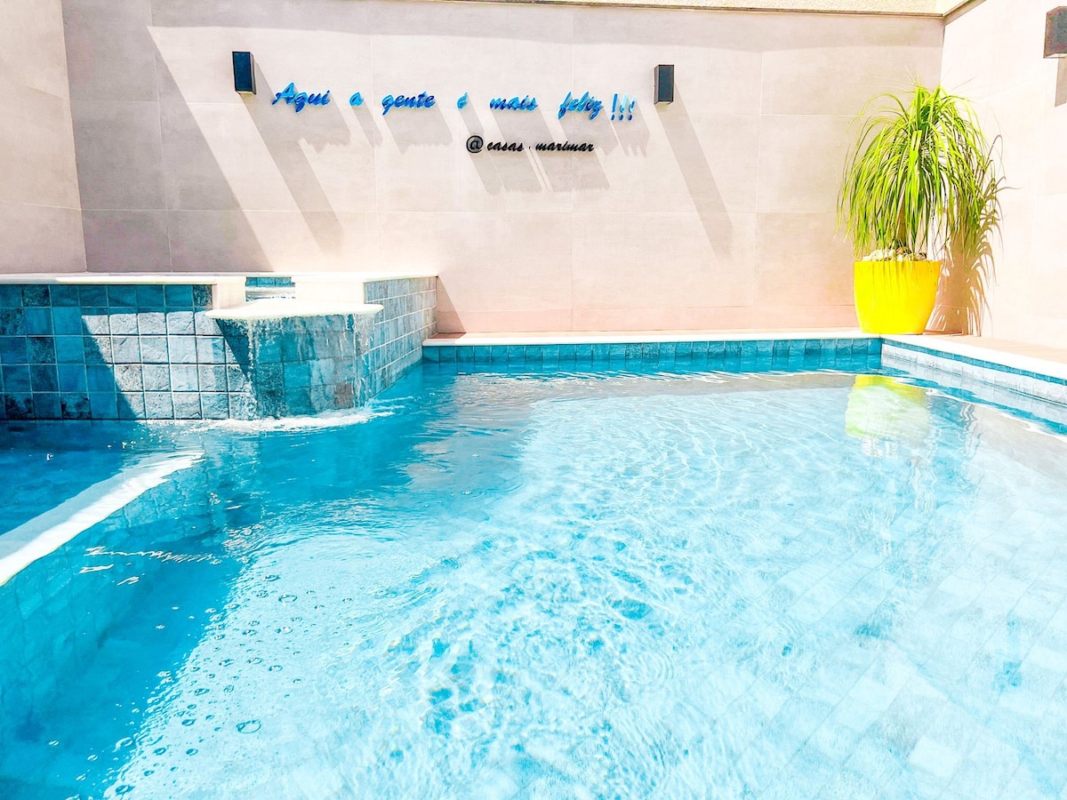 A private swimming pool features clear blue water, complemented by a small waterfall and steps leading into the water. A vibrant yellow plant pot adds a pop of color to the area, enhancing the refreshing ambiance.