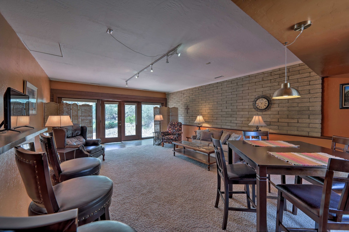 A spacious living area features cozy seating with an armchair, sofa, and dining table, illuminated by soft lighting. Floor-to-ceiling glass doors allow natural light to enter, offering views of the outdoor space. Textured brick walls provide a rustic backdrop for the room.