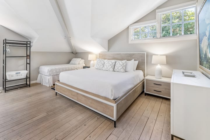 Separate detached guest cottage featuring a vaulted ceiling, cozy natural light, and two comfortable beds for a relaxing retreat.