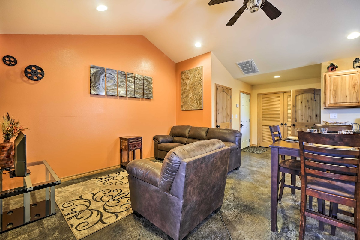 A living area features an open layout with a cozy seating arrangement including a leather sofa and armchair. Decorative wall art adds depth to the orange walls, while a ceiling fan provides comfort. A dining table for four is positioned nearby, enhancing the functional space.