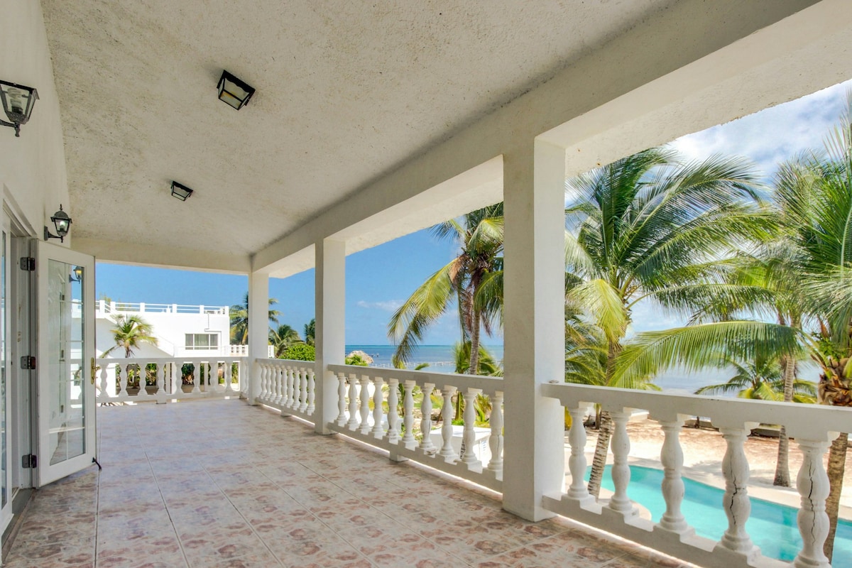 A spacious balcony features elegantly styled railings, providing a panoramic view of the palm trees and ocean. Natural light fills the area, highlighting the tiled floor. The inviting ambiance is complemented by comfortable seating arrangements, creating an ideal spot for relaxation.