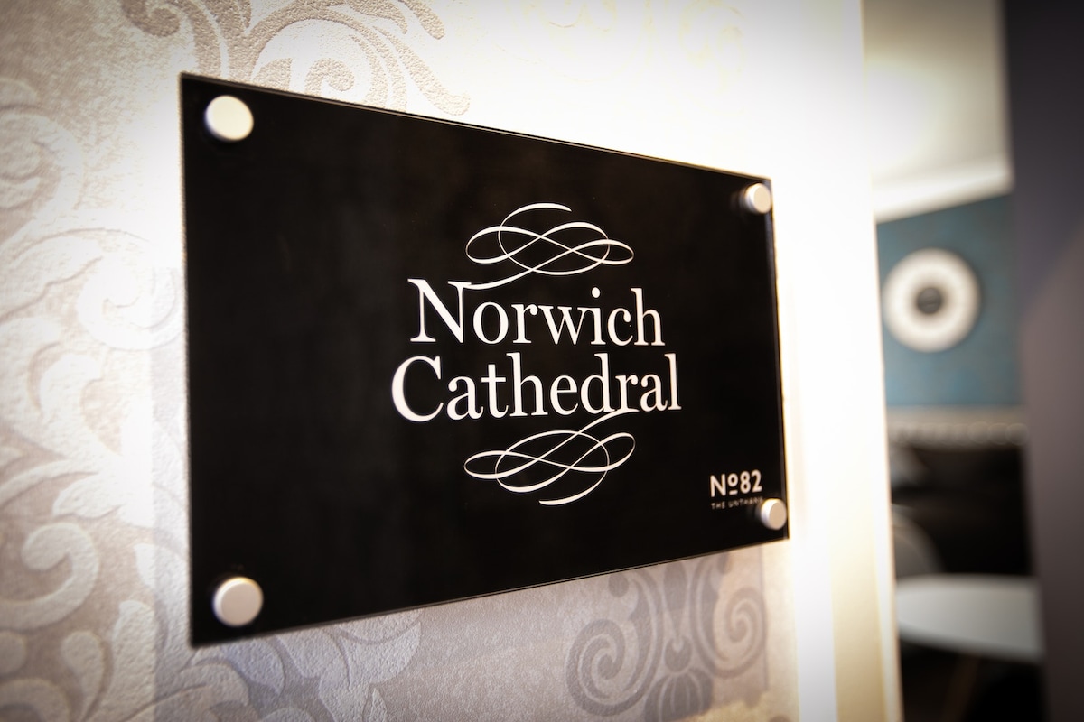 A decorative sign displays the name 'Norwich Cathedral,' elegantly mounted on a textured wall. The design features a mix of classic and contemporary elements, with a polished finish that complements the surrounding decor.