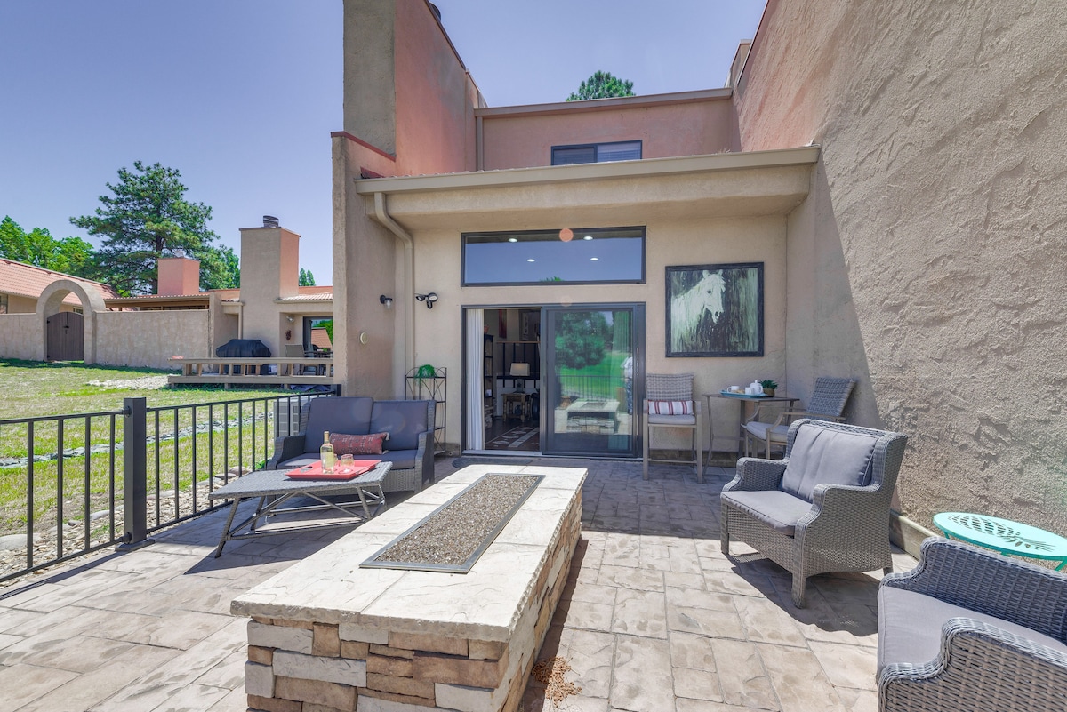 A private patio area is showcased, featuring comfortable seating arrangements and a fire pit made of stacked stone. Large sliding doors lead to the interior, while the surrounding landscape includes greenery and additional outdoor seating.