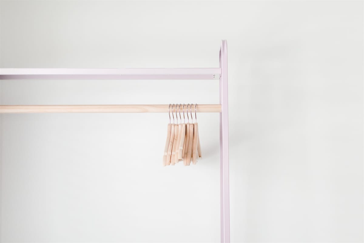 A minimalist clothing rack features a light wooden bar supported by a soft purple frame. Several wooden hangers are neatly arranged on the bar, providing a practical storage solution.