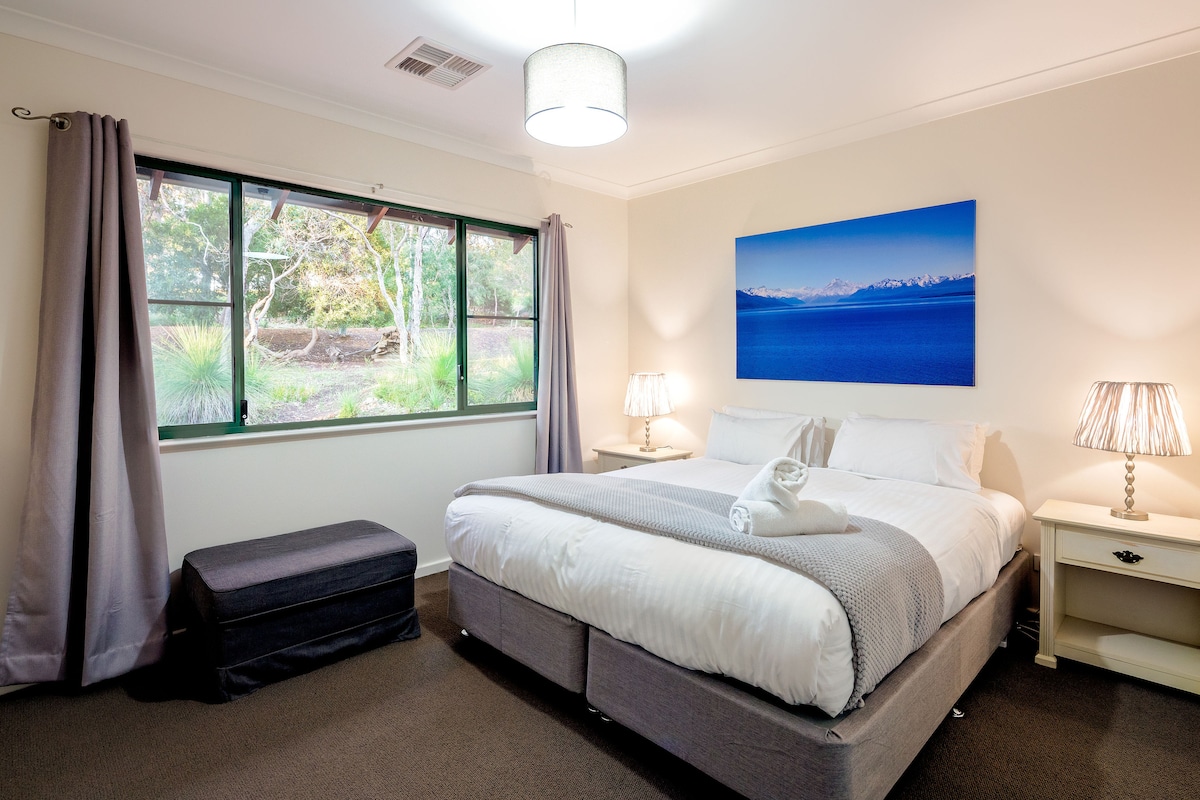 Починете във втората спалня с двойно легло king size, където голям прозорец предлага успокояваща гледка към околните храсти, идеални за спокойно уединение.