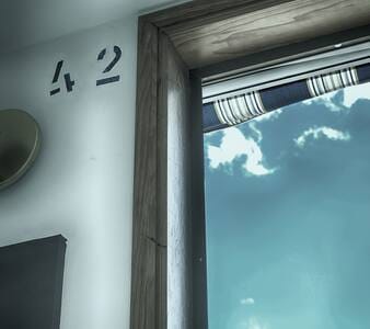 The image captures a corner of the room where a wooden window frame opens to reveal a bright sky with scattered clouds. The number '42' is displayed on the wall beside the window, indicating the studio's identification.