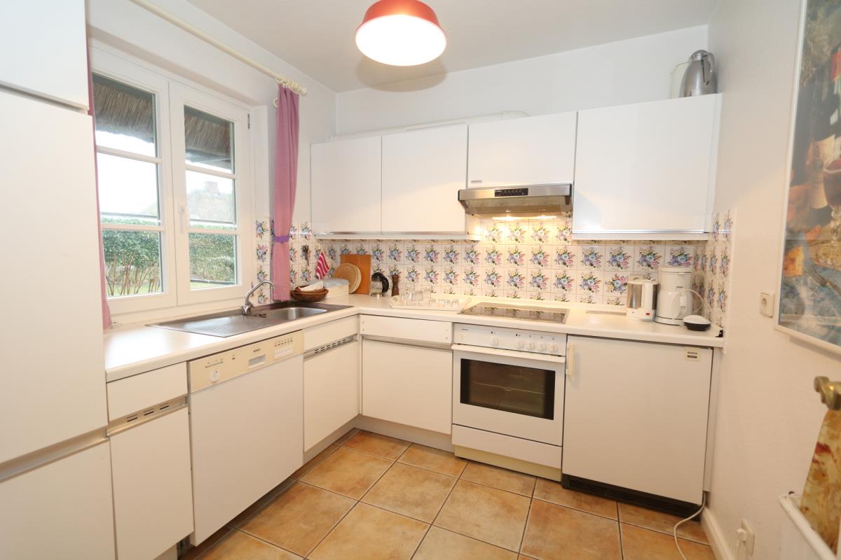 A bright kitchen is equipped with modern appliances, including an oven and a dishwasher. The cabinetry features a clean, white design with floral backsplash tiles. Ample counter space offers room for meal preparation, while natural light enters through a nearby window.