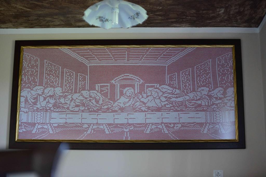 A large framed artwork depicting a reinterpretation of 'The Last Supper' is displayed on the wall. The composition features a series of pixelated figures in a muted color scheme, creating a unique visual experience within the room.