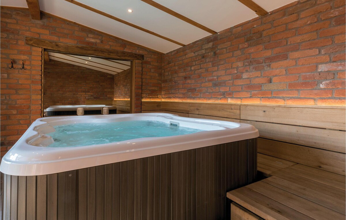 A well-appointed jacuzzi is positioned against a backdrop of rustic red brick walls, featuring wooden benches that provide additional seating. Soft lighting enhances the inviting atmosphere within the wellness area, creating a space for relaxation.