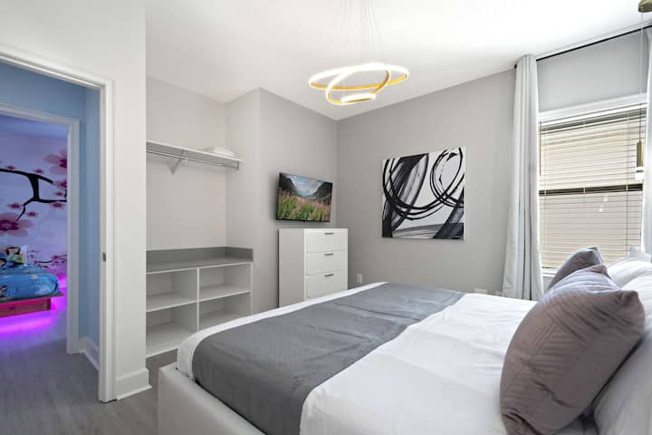 Chambre élégante avec lit queen size, art moderne, télévision et rangement ouvert. 