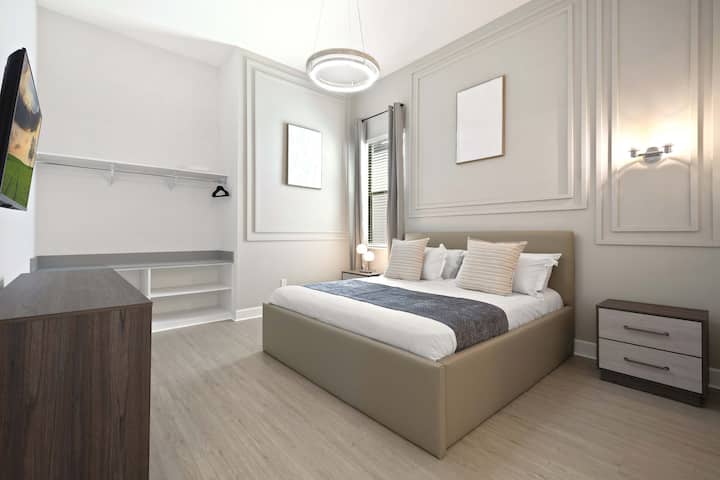 Chambre élégante avec lit queen size, moulures décoratives, éclairage design et garde-robe ouverte. 