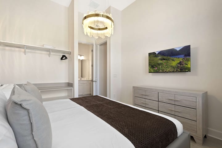 Chambre lumineuse et moderne avec un lit queen size, un lustre chic et une télévision à écran plat. 