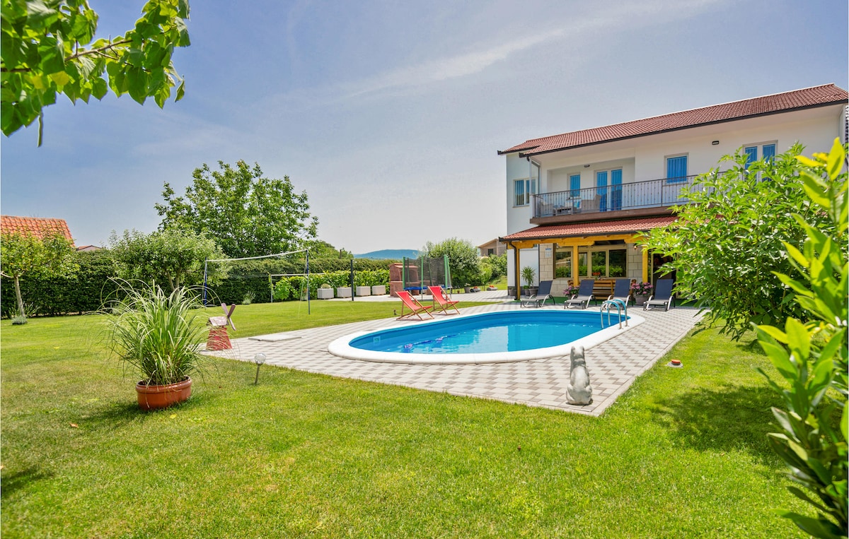The image captures a spacious backyard featuring a private pool surrounded by lounge chairs. Lush greenery and well-maintained grass create a serene environment. The two-story house with a balcony overlooks the yard, enhancing the outdoor setting.