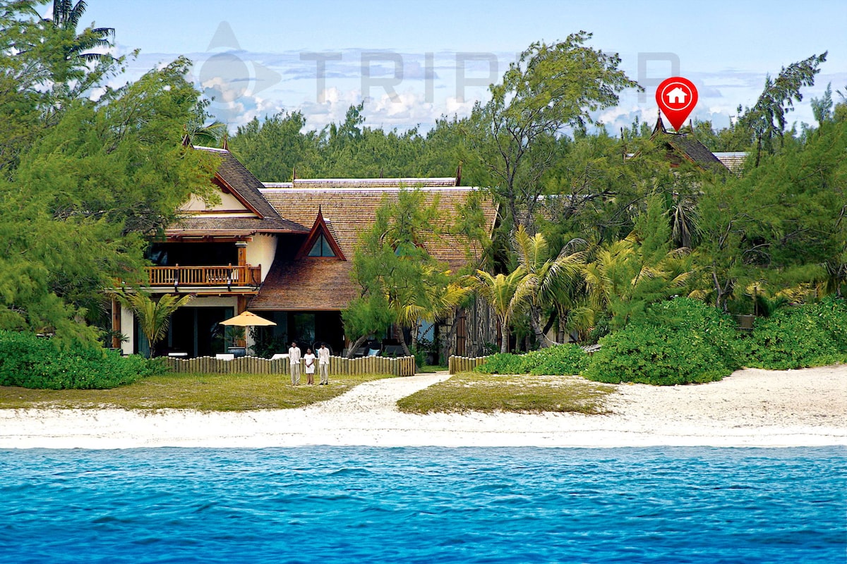 This beachfront villa, framed by lush greenery, highlights a blend of Balinese and Mauritian architecture. The structure features a natural palette, large windows, and balconies providing sea views. A private path leads directly to the white-sand beach and turquoise lagoon.