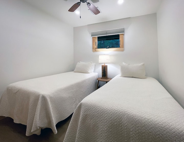 Chumba cha kulala chenye vitanda viwili vya mapacha, feni ya dari na mapambo ya mbao mepesi yanayofanya kuonekana safi na yenye hewa safi.