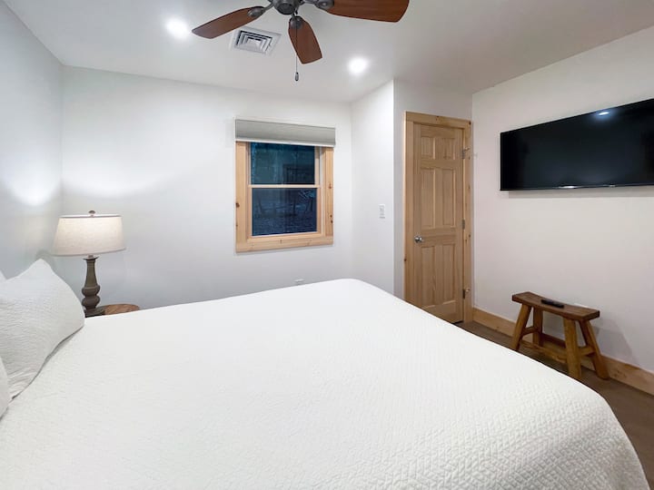 Chumba kipana cha kulala chenye kitanda cha mfalme, runinga na mapambo ya kisasa ya mbao yanayotoa mazingira tulivu na ya kustarehesha.