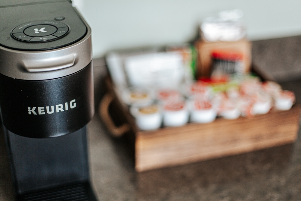 A Keurig coffee maker is prominently displayed on a countertop, with a tray of various coffee pods neatly arranged in the background. The setup emphasizes convenience for guests looking to enjoy a warm beverage during their stay.