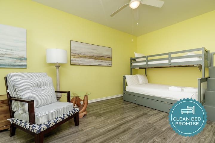 Your cheerful yellow bedroom features a cozy bunk bed and reading chair with coastal artwork for relaxing family stays.