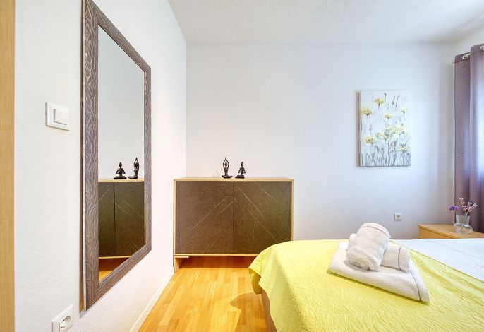 تتميز غرفة النوم المريحة هذه بأرضيات خشبية دافئة وإضاءة ناعمة ومرآة كبيرة تضيف السحر والضوء. تضفي خزانة الملابس المزخرفة والأعمال الفنية المزخرفة بالزهور طابعًا مميزًا، بينما تضفي المناشف المطوية بعناية على السرير لمسة ترحيبية.