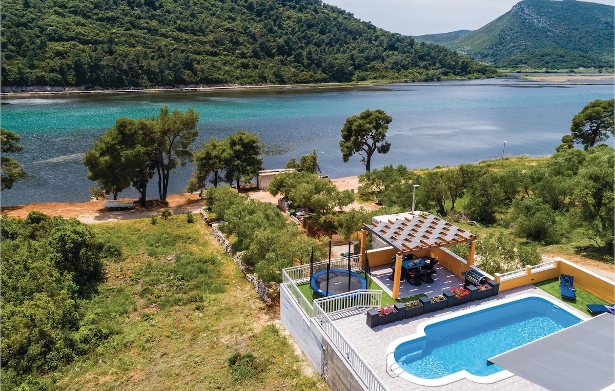 An aerial view of the property showcases a private pool surrounded by green landscaping, with a covered seating area nearby. The tranquil water reflects the greenery and mountains in the distance, creating a peaceful outdoor setting that invites relaxation.