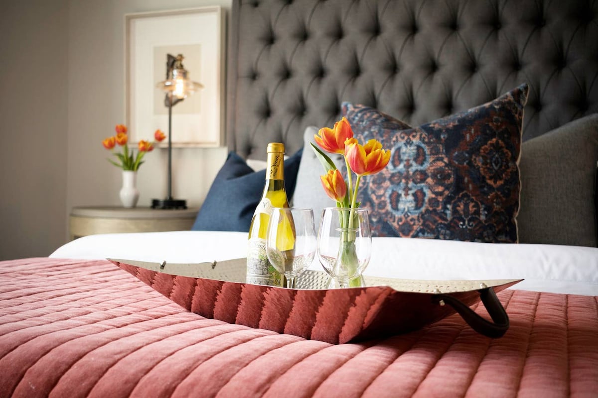 - El cabecero acolchado y las almohadas estampadas crean un ambiente cálido y exclusivo para disfrutar de noches de descanso - La bandeja decorativa con champán y tulipanes crea el ambiente perfecto para una estancia relajante - Las texturas de diseño y la iluminación suave añaden elegancia y encanto a este acogedor espacio