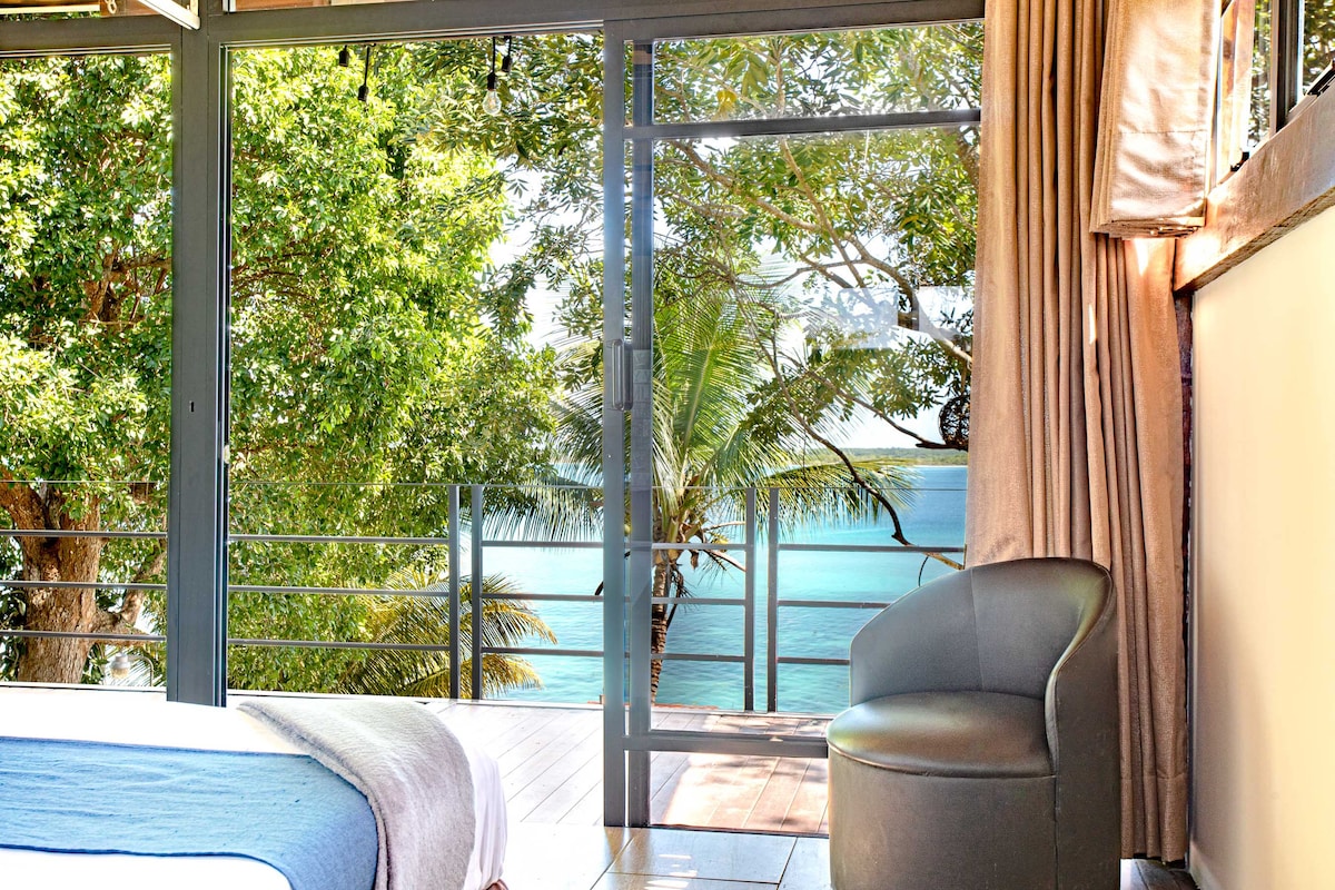 Замислете светла и удобна главна спална соба, декорирана во меки тонови. Од креветот се гледа балконот, каде што се отвораат стаклените врати за да влезе свеж ветер. Погледот на лагуната Бакалар го одзема здивот: нејзините интензивно сини води се вклопуваат со зеленилото