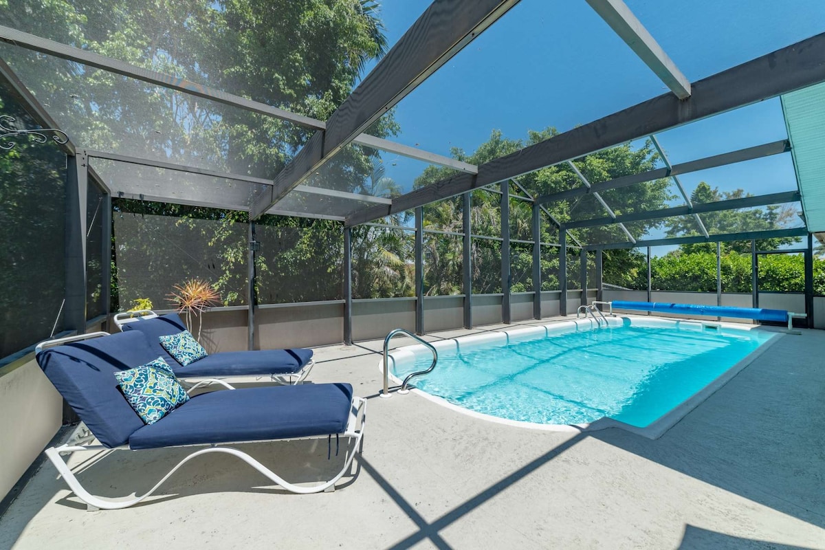 A screened-in pool area showcases a refreshing swimming pool surrounded by concrete flooring. Two lounge chairs with blue cushions are positioned nearby, inviting relaxation. Lush greenery is visible through the screen, providing a serene backdrop to the private escape.