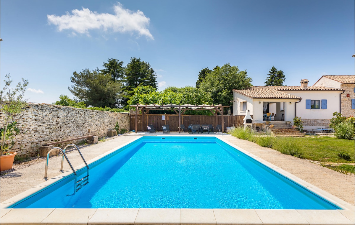 A private outdoor pool with a clear blue surface is surrounded by a spacious patio area. Lush greenery and trees border the yard, while a stone wall adds privacy. Sun loungers are positioned nearby, providing a relaxing space for guests to enjoy.