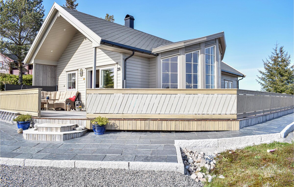 The vacation home is presented with a light exterior and large windows, inviting natural light into the interior. A spacious terrace is shown, bordered by a wooden railing and adorned with potted plants, offering an area for relaxation outdoors.