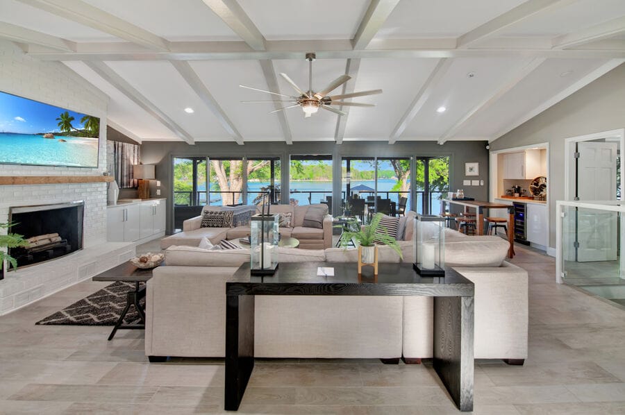 An open living area is highlighted by comfortable seating arrangements, offering a view of Lake Norman through large windows. A modern ceiling fan circulates air, while a cozy fireplace and tasteful decor enhance the inviting atmosphere. Natural light fills the space, creating a bright ambiance.