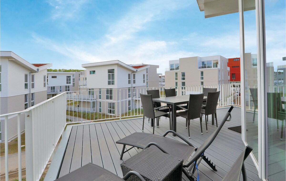 A spacious roof terrace features a table with four chairs and two lounge chairs, offering ample room for relaxation. Nearby, modern buildings are seen against a clear blue sky, providing a tranquil atmosphere for outdoor enjoyment.