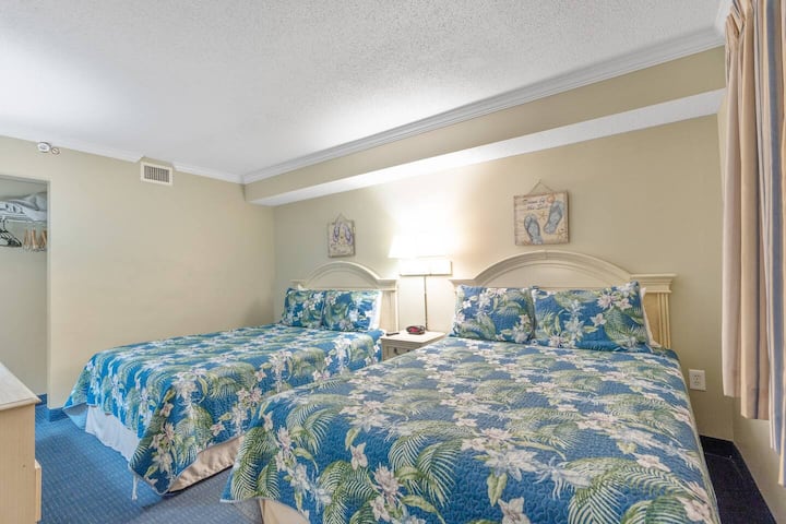 Prostrana spavaća soba s dva udobna bračna kreveta s posteljinom s tropskim motivima, nježnim osvjetljenjem i opuštajućom atmosferom.