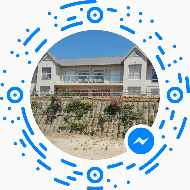 A modern two-story building is featured, with a balcony overlooking a landscaped area filled with colorful flowers. Bright blue skies complement the structure, which is elevated above the surrounding terrain, providing an unobstructed view of the outdoor space.