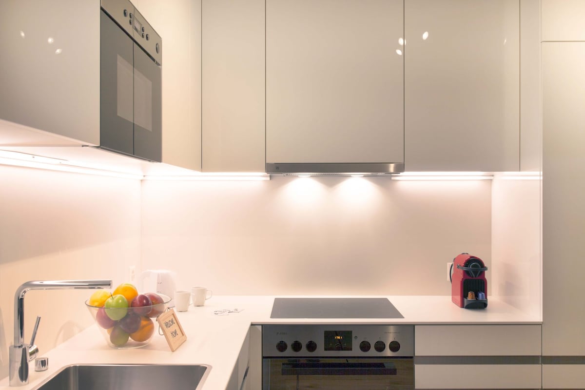 A modern kitchen area features sleek cabinetry with integrated appliances. A bowl of colorful fruit adds a touch of vibrancy. A coffee machine sits on the countertop, with a cooktop and oven conveniently accessible beneath a stylish exhaust hood.