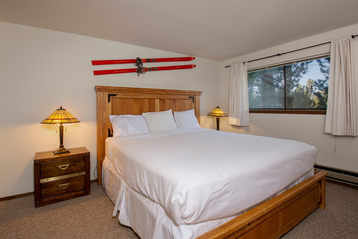 Versinke in frische weiße Bettwäsche auf deinem komfortablen Kingsize-Bett, mit warmen Holzmöbeln und Skimotiven, die einen gemütlichen Rückzugsort in den Bergen schaffen.